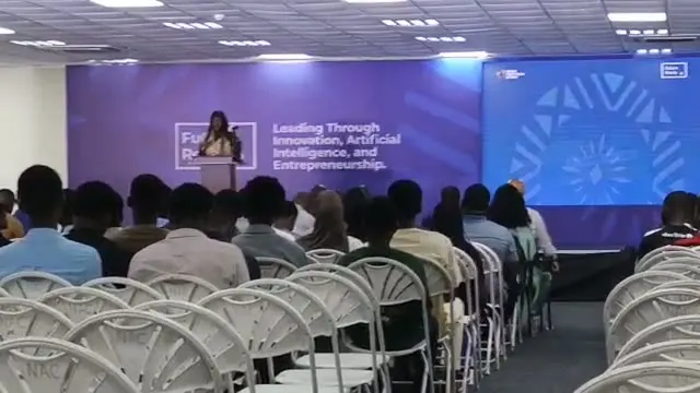 Speaker addressing a conference audience in front of a purple stage backdrop